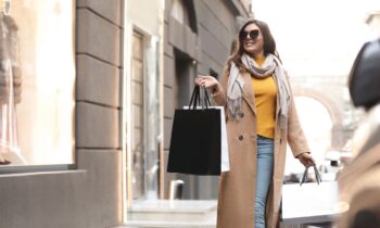 A mystery shopper, walking outside a store front, holding shopping bags.